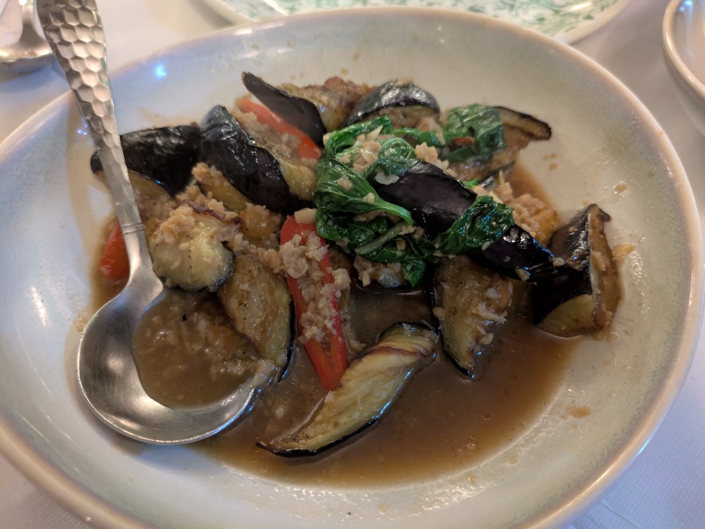 Slices of aubergine, very fine vegan mince, and Thai basil leaves in a light sauce