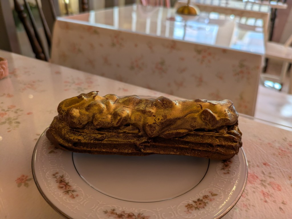 A side view of a chocolate eclair with a bumpy gold topping
