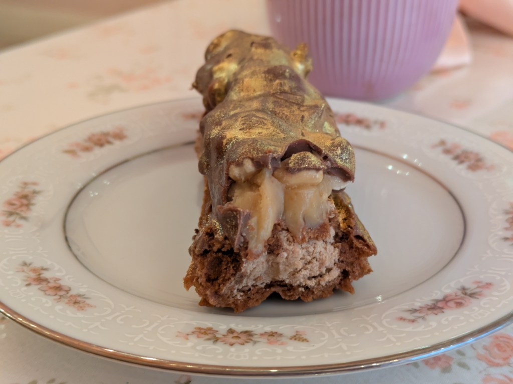 A cross section of the eclair which shows it is filled with a chocolate cream, topped with caramel and nuts, and coated in chocolate
