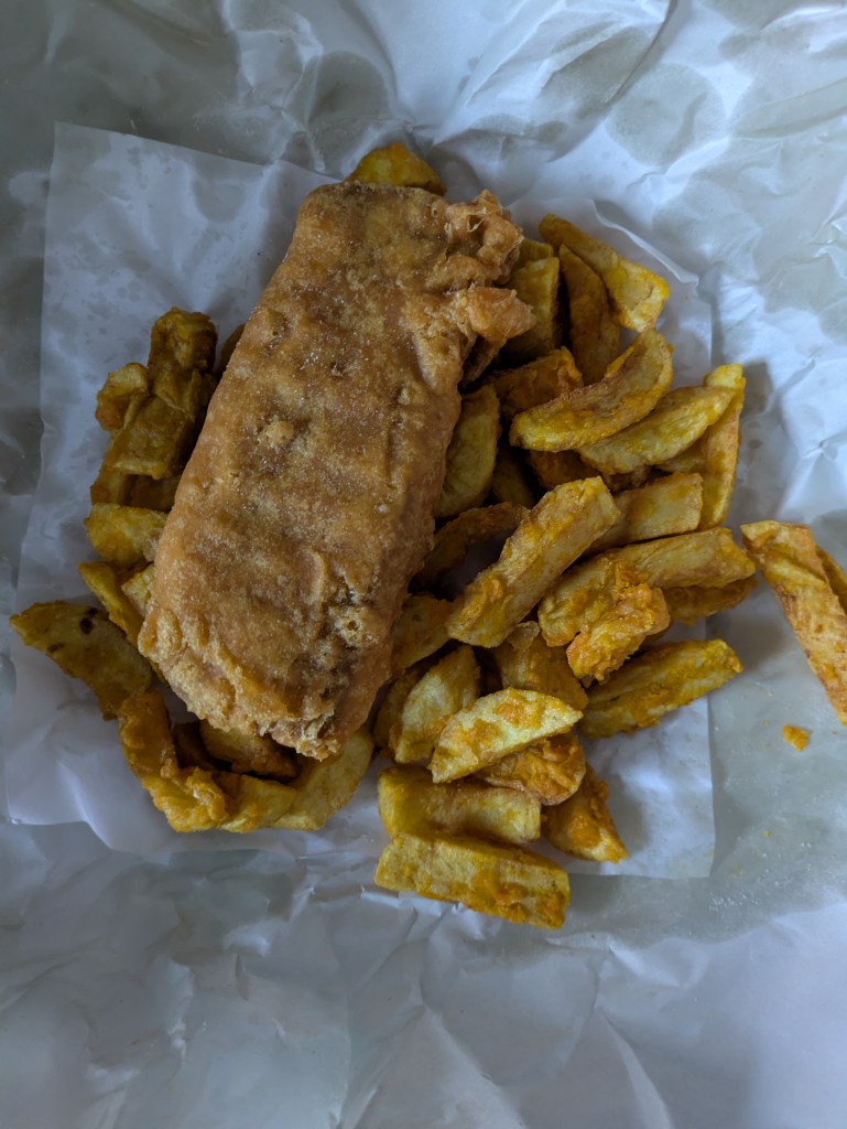 Battered fish with battered chips, that have orangey batter on them