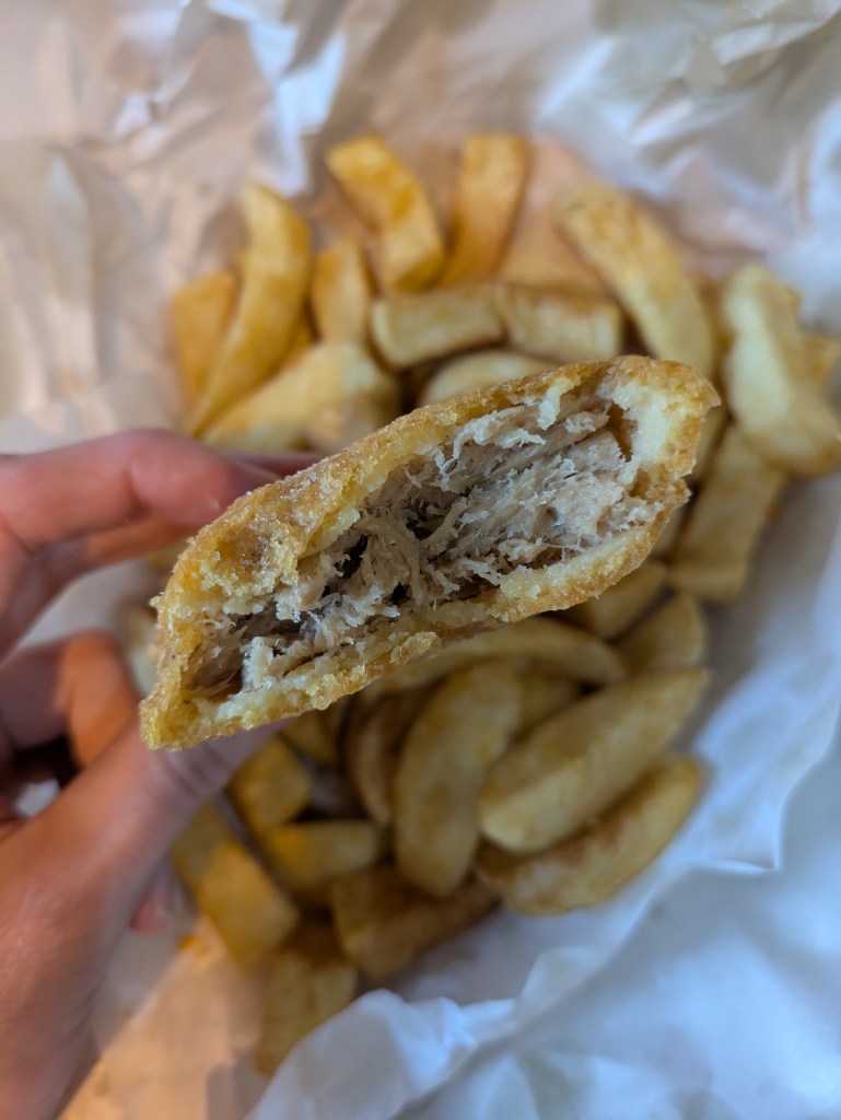 A look inside the battered fish, showing quite a flaky, stringy texture and a crispy coating