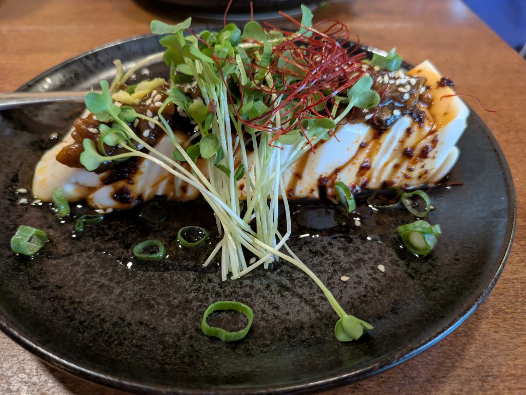 Slices of silken tofu topped with a brown sauce and garnished with greens