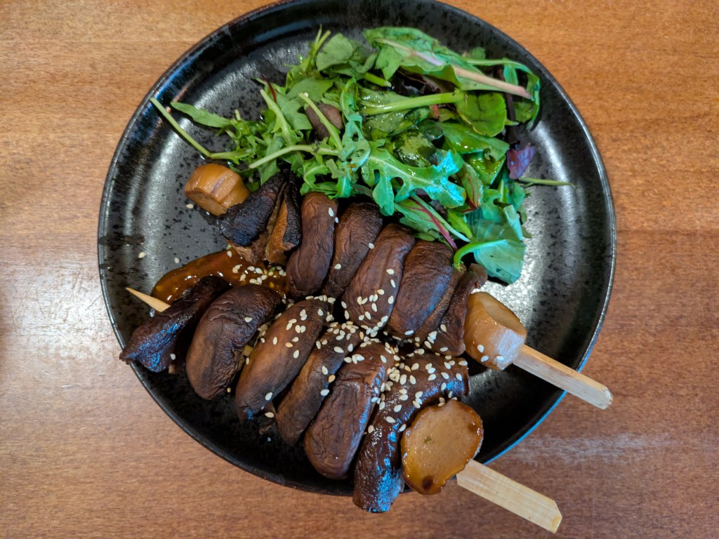 Two skewers with large mushroom pieces, served alongside a salad