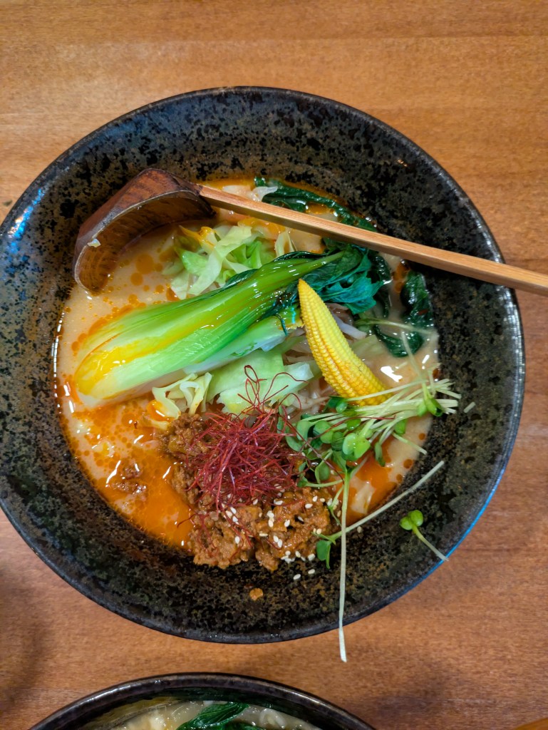 A bowl of ramen with a creamy broth and chilli oil, a mound of vegan mince, a piece of baby sweetcorn and a large pak choi