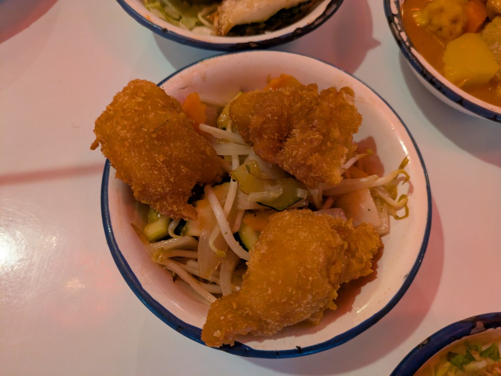 Three battered prawns on top of a small bowl of stir fried vegetables 
