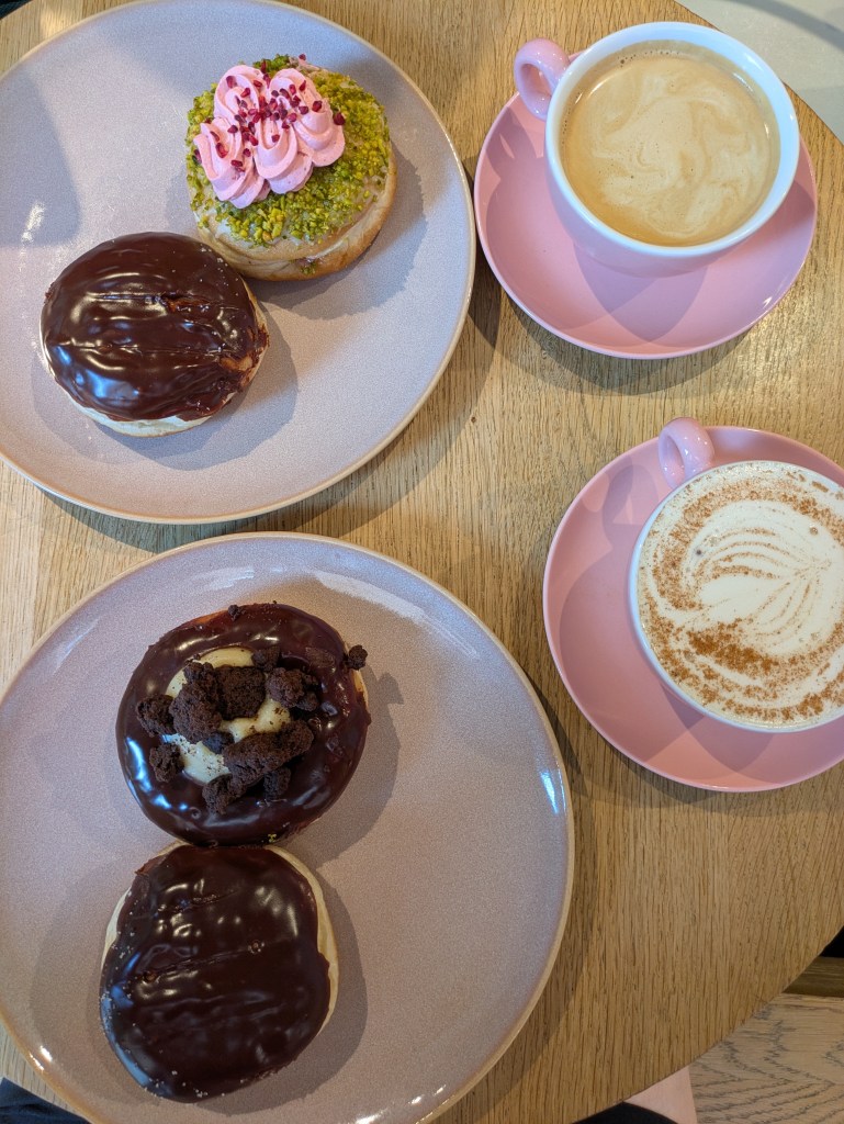 Two plates of donuts and two mugs of milky hot drinks