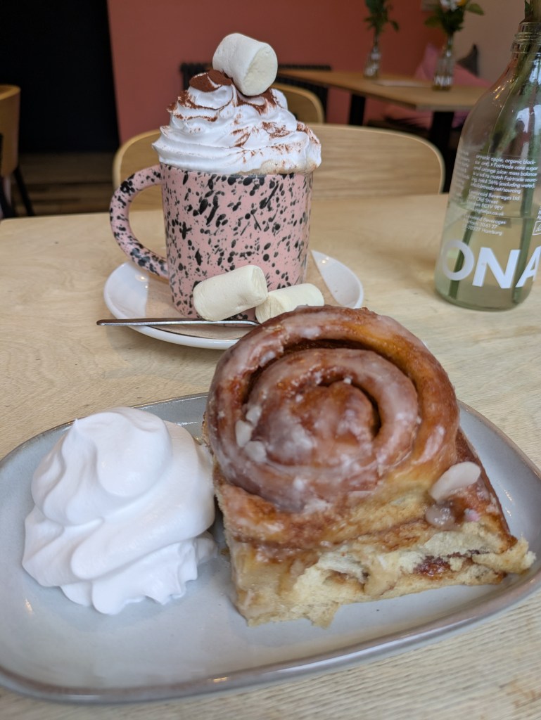 A mug of hot chocolate topped with cream and marshmallows, and a cinnamon roll