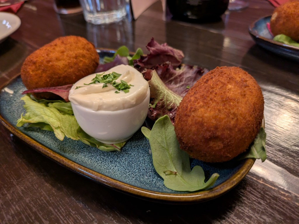 Two crispy looking arancini with a white dipping sauce and some side salad