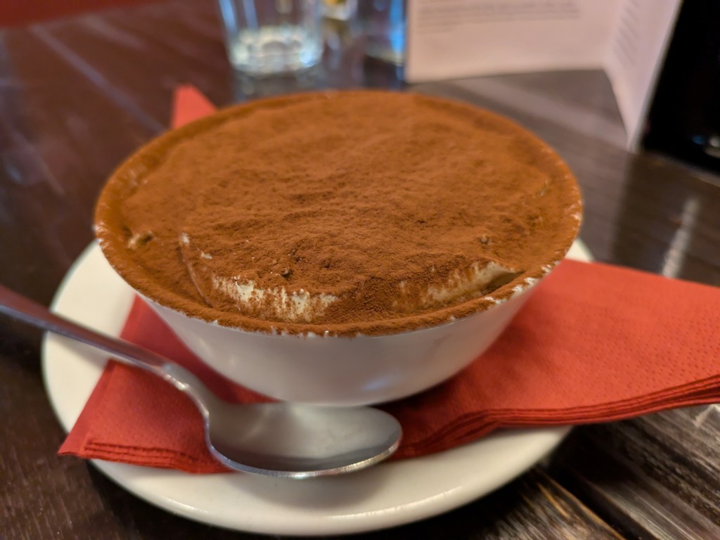 A small bowl of tiramisu, topped with a heavy dusting of cocoa powder
