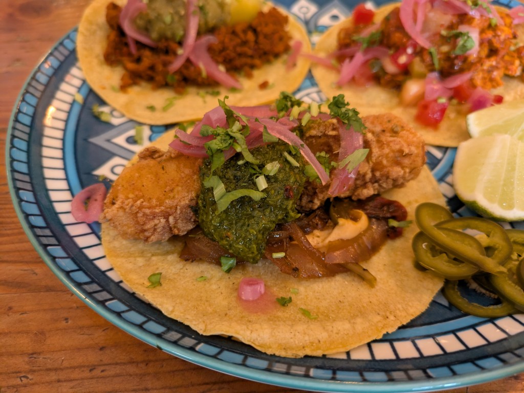 A taco filled with a large crispy slab of pineapple and garnished with sauces