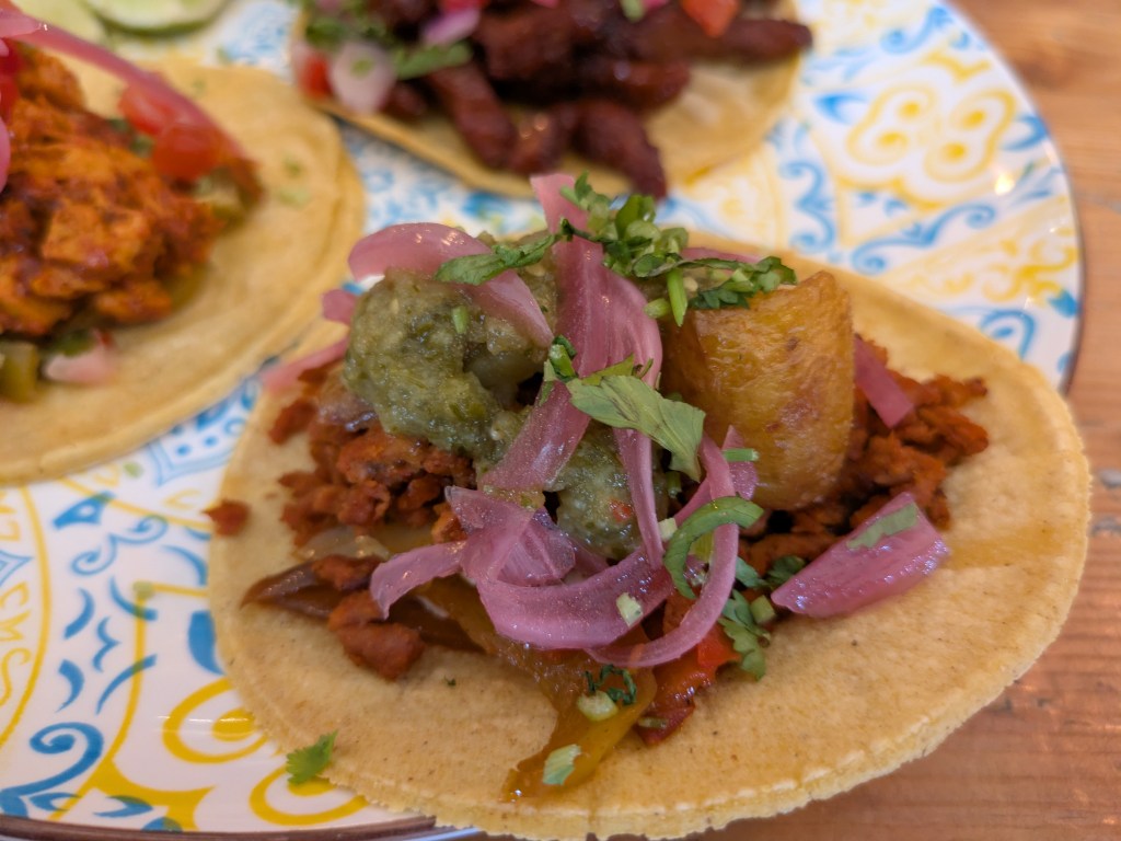A taco filled with mince, a chunk of potato, and avocado cream