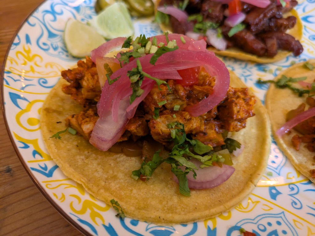 A taco with a chicken filling garnished with pickled red onions and chives