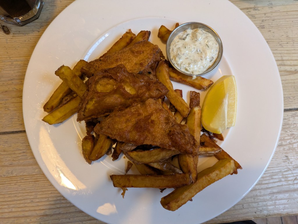 A portion of chips topped with some triangles of battered tofu, alongside some tartar sauce 