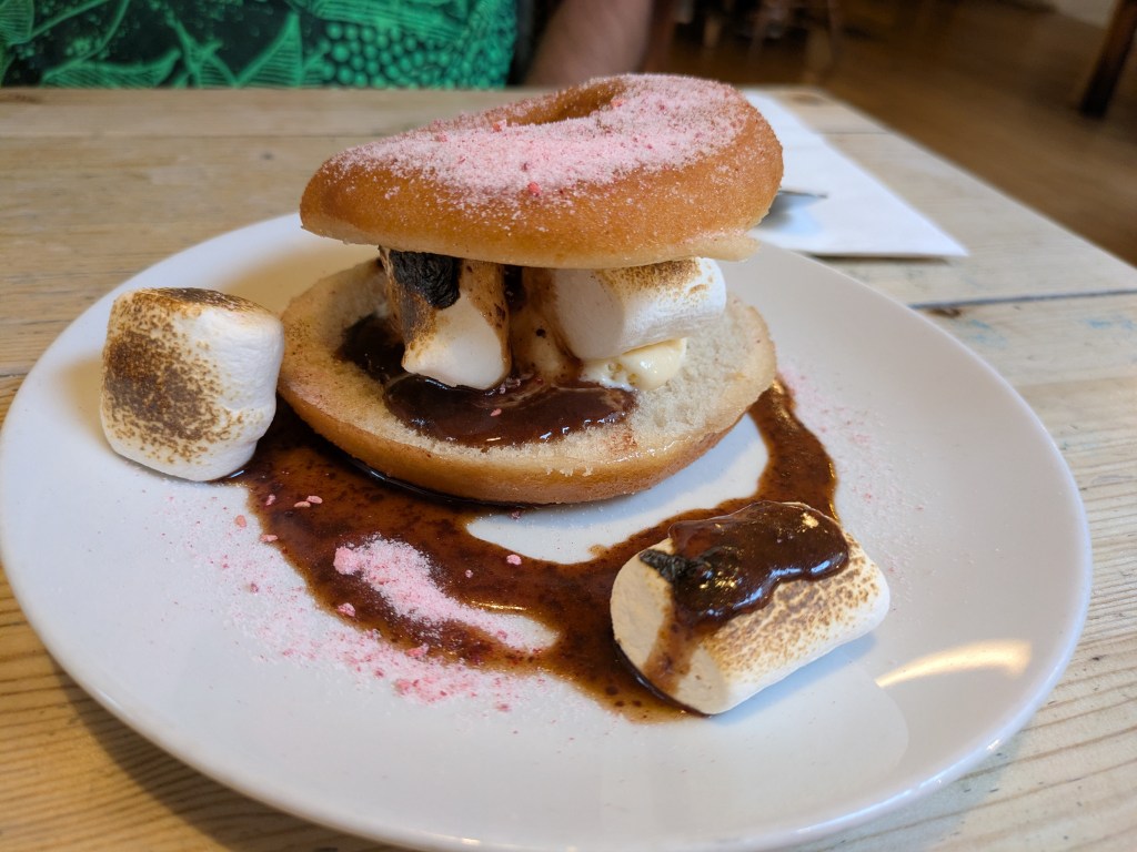 A ring donut cut in half and sandwiched with torched marshmallows and chocolate sauce