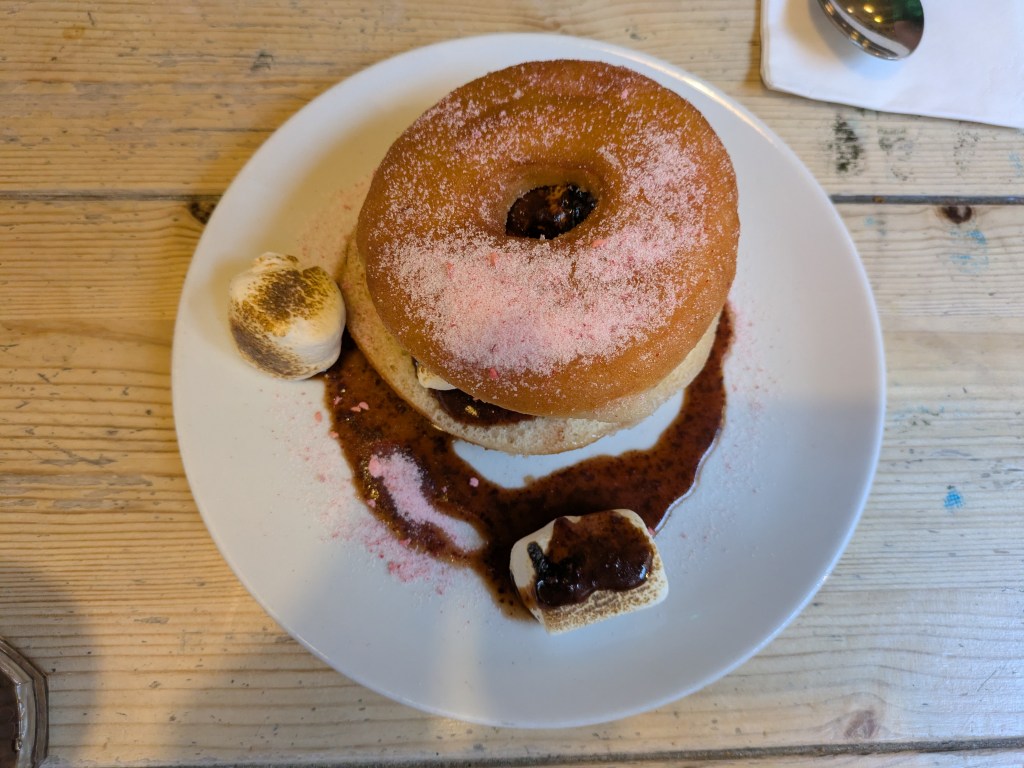 A ring donut cut in half and sandwiched with torched marshmallows and chocolate sauce