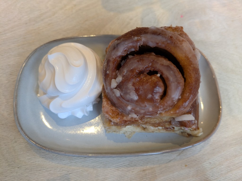 A cinnamon roll with a swirl of whipped cream on the side