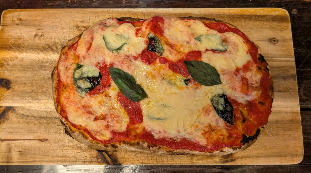 A pinsa topped with tomato sauce, loads of melted cheese, and some fresh basil leaves