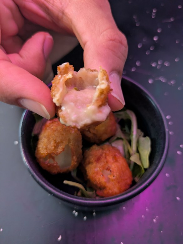 Four deep fried cheese balls, one of them open to show the oozing cheese