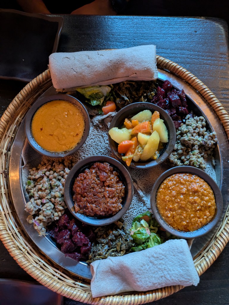 A large tray covered with injera topped with various vegetable dishes and a few hot vegetable dishes in small bowls