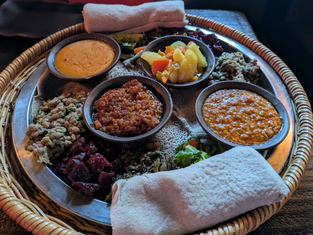 A large tray covered with injera topped with various vegetable dishes and a few hot vegetable dishes in small bowls