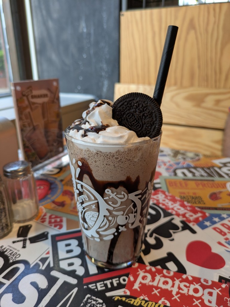 A big glass of chocolate milkshake with chocolate sauce around the glass, topped with whipped cream and an Oreo 