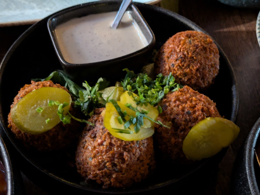 Four crispy falafels garnished with pickles and herbs and served with a tahini dipping sauce 