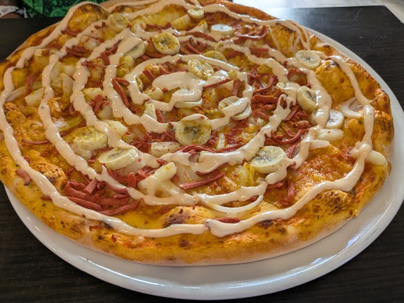 A pizza with lots of toppings including round banana slices, covered with a spiral of sauce
